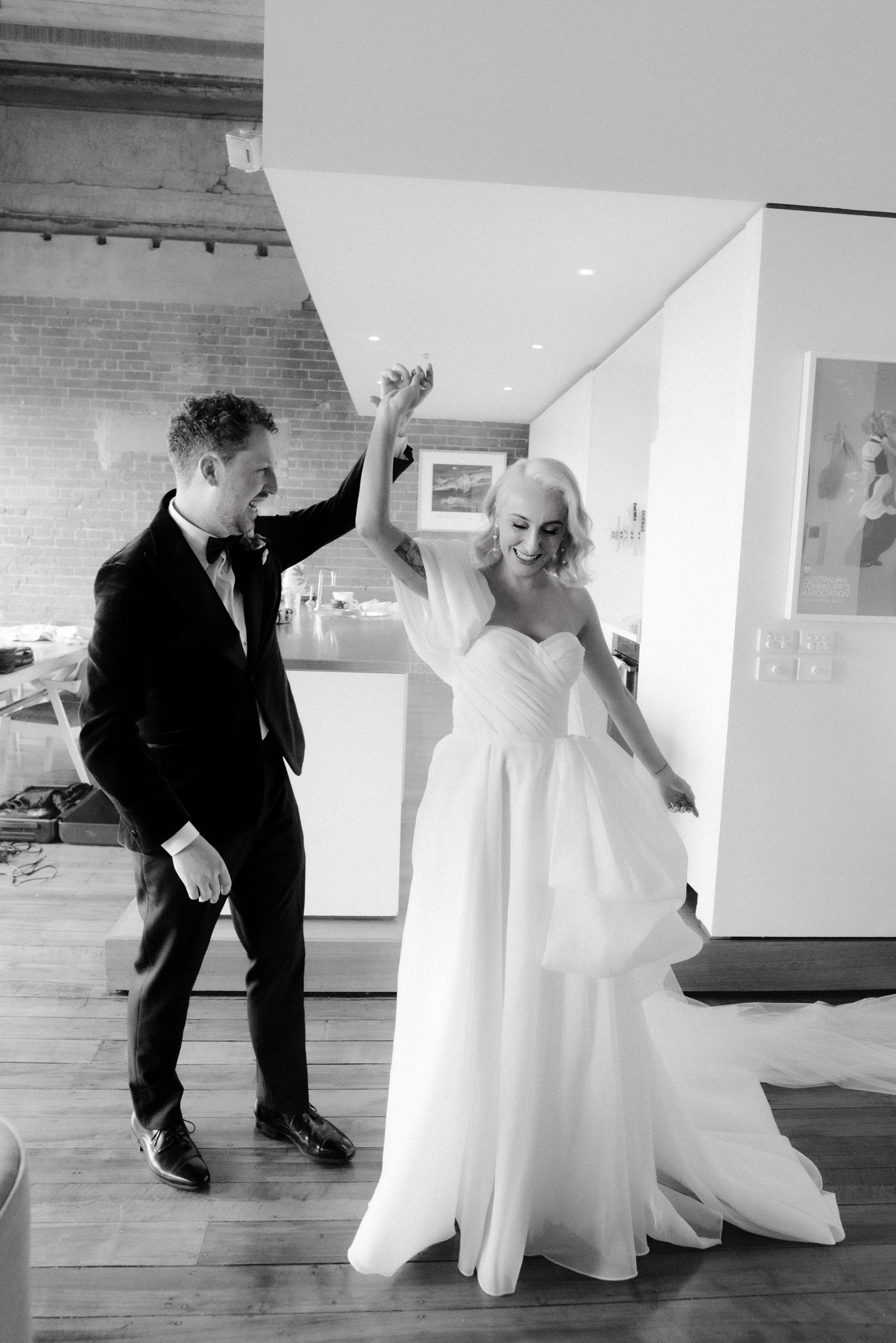 A black and white film photo of a groom twirling his bride after seeing her in her dress for the first time.