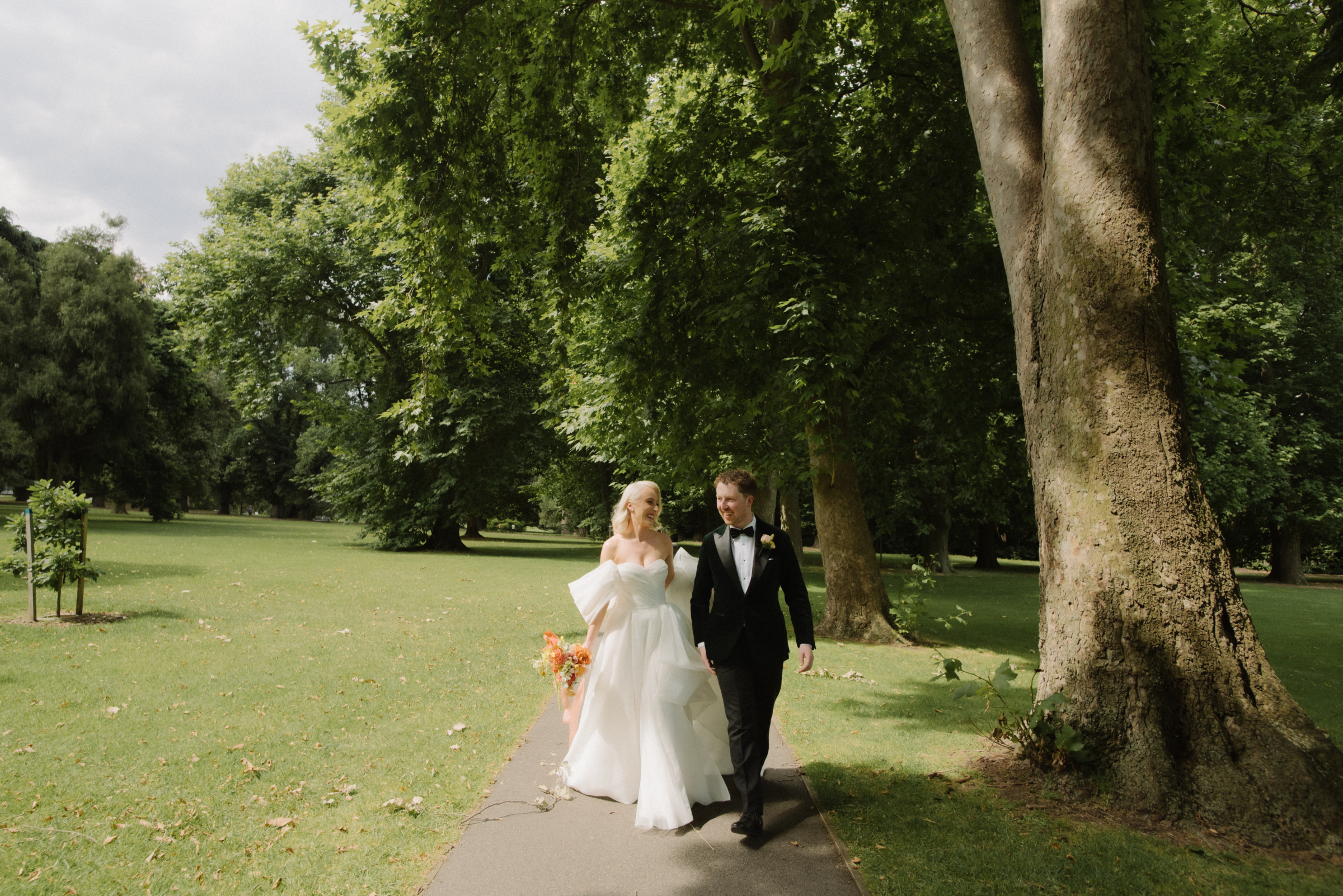 A bride and groom walking on a path at Fitzroy Gardens during their photo portrait session.