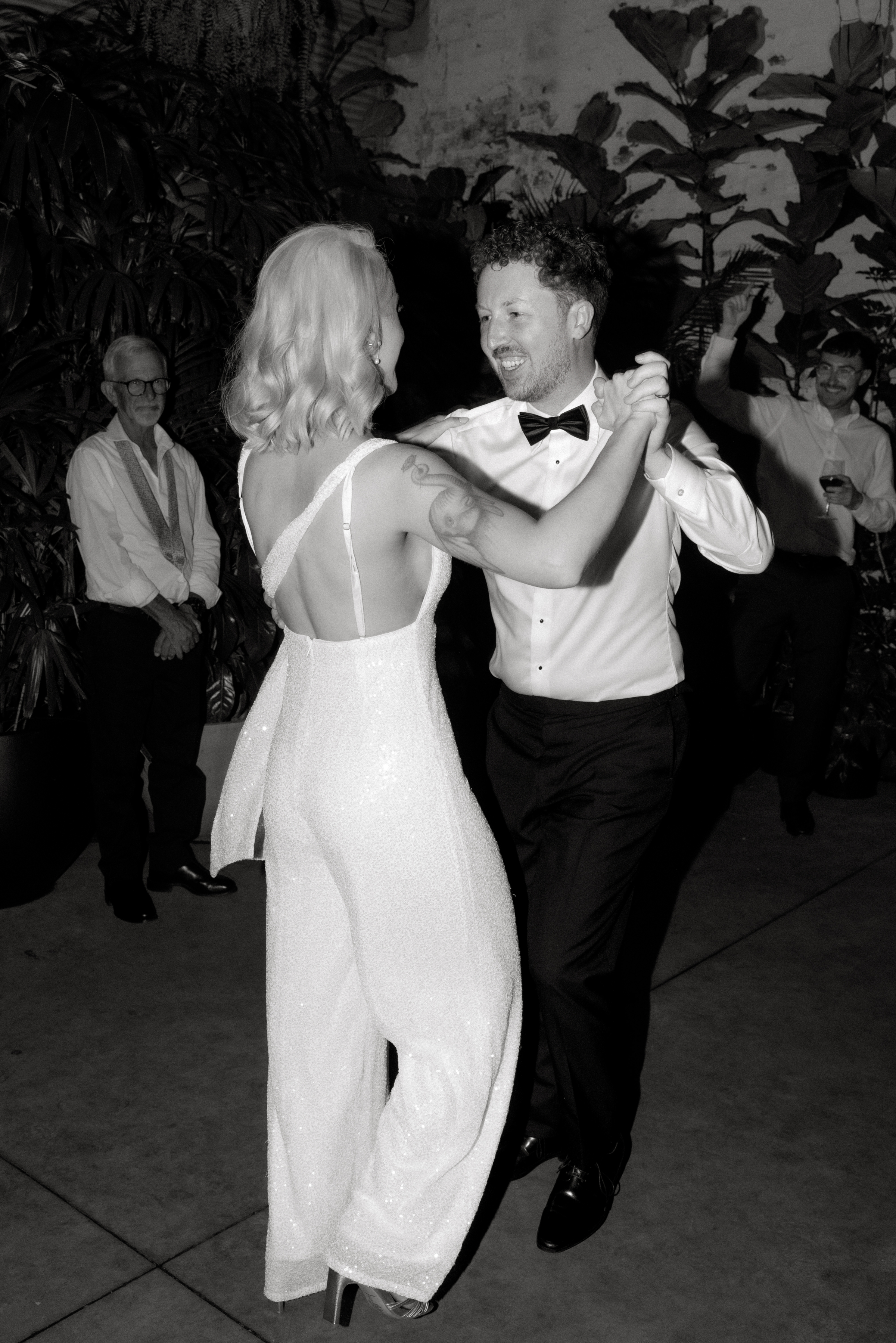 A black and white photo of a bride wearing a white sequinned jumpsuit during her first dance with the groom at Glasshaus Inside in Cremorne, Melbourne.