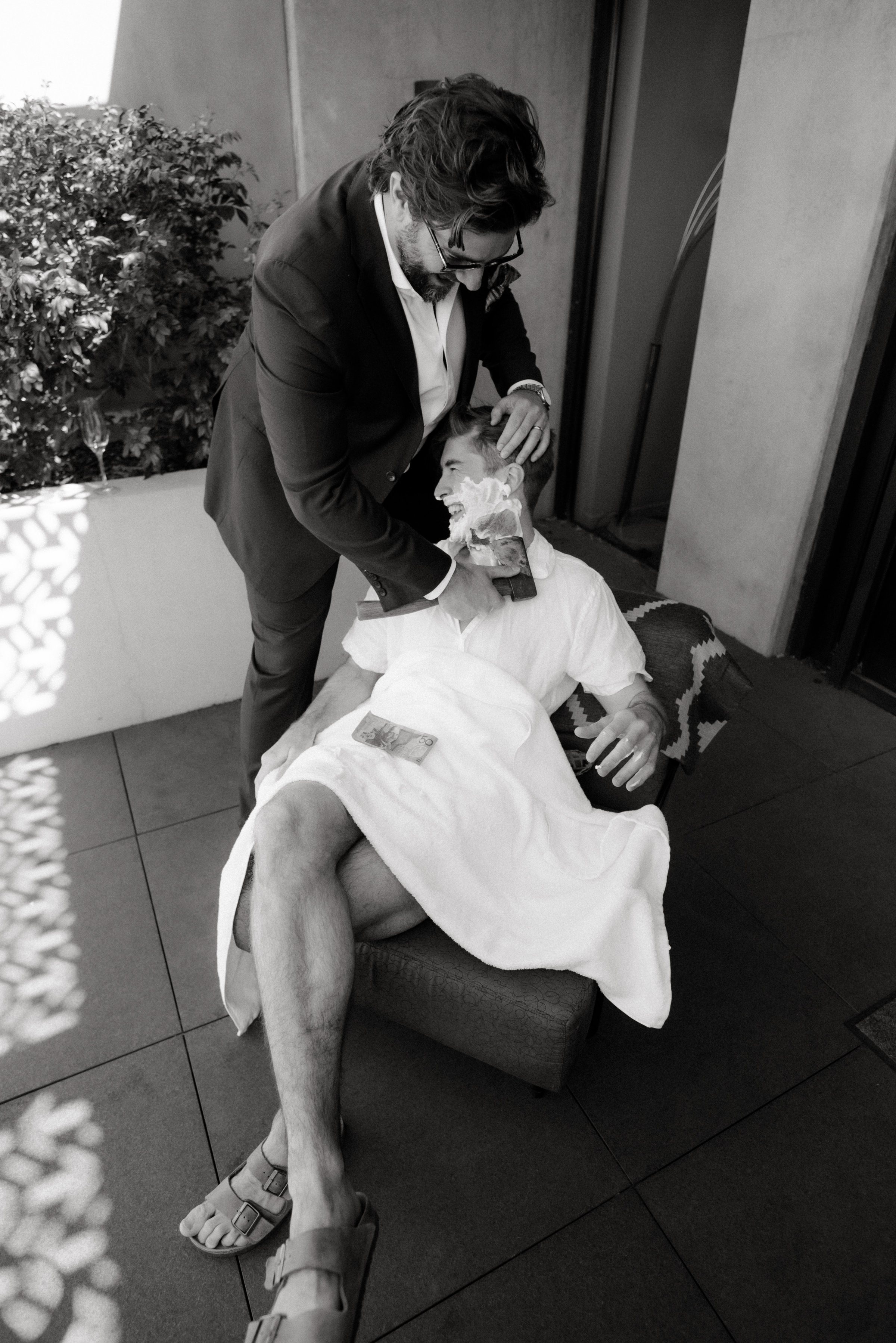 A black and white photo of a groom being shaved with a tomahawk.