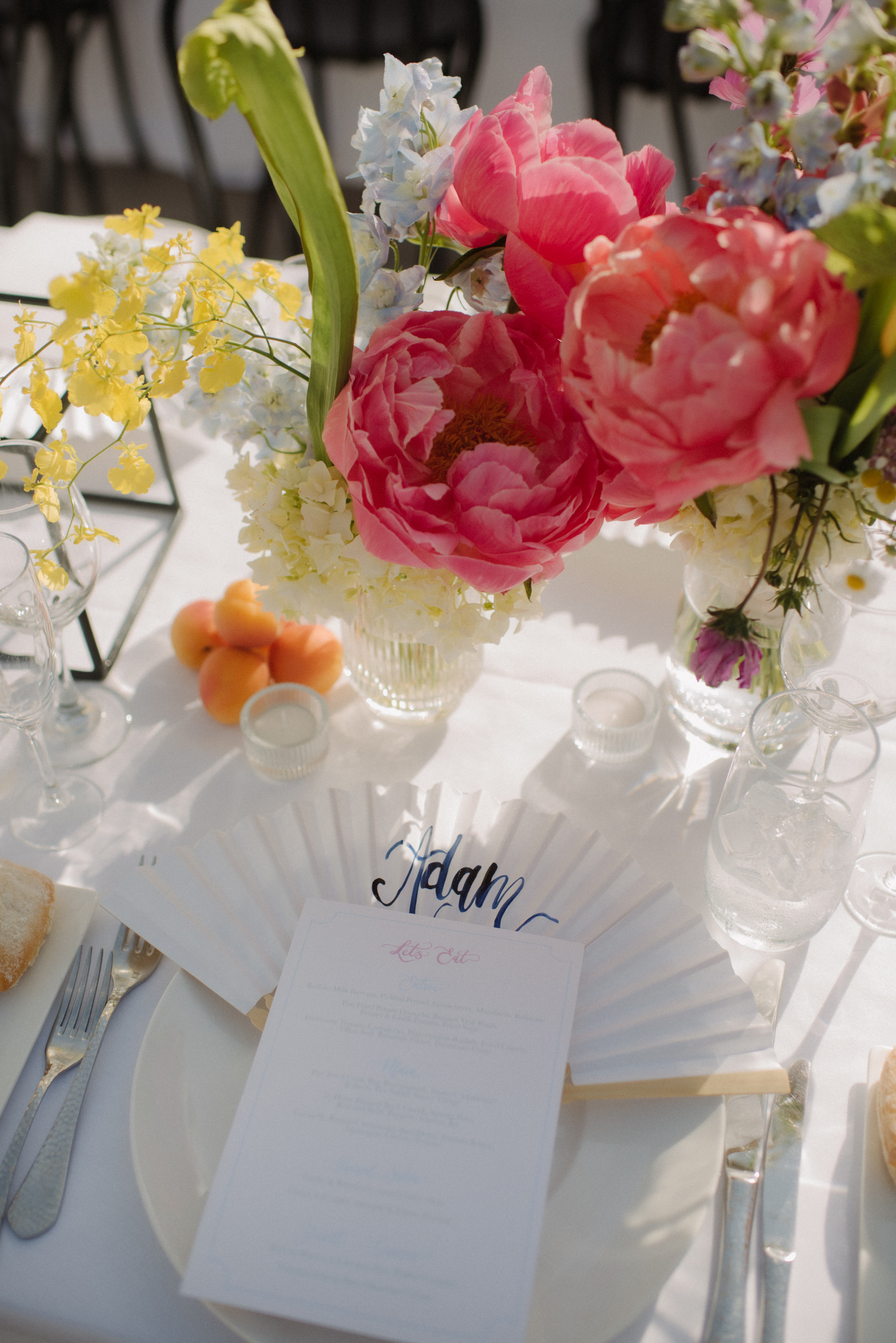 A custom named fan sits on a table amongst stone fruit and flowers.