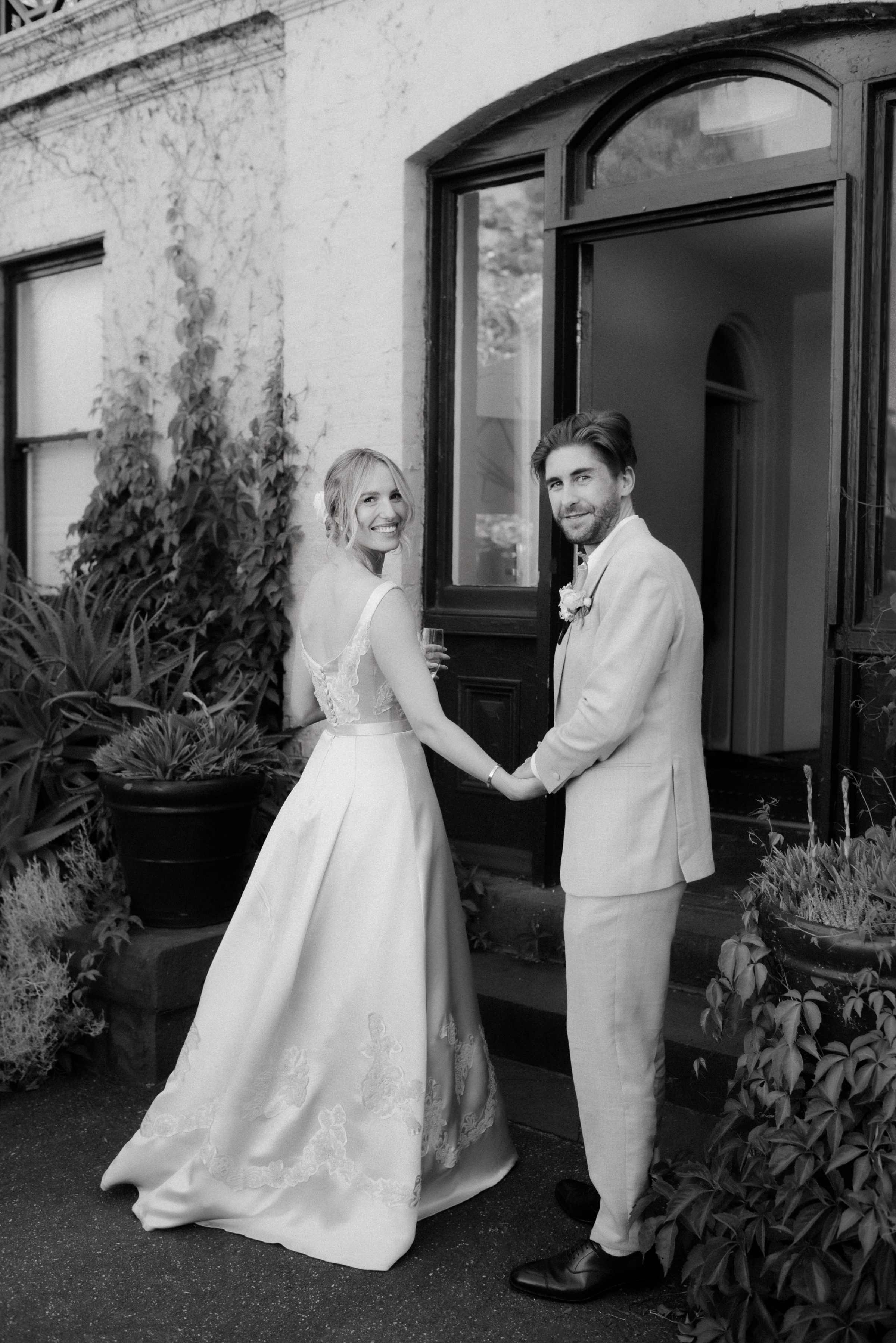 A black and white photo of a bride and groom looking back as they enter Gardens House, Melbourne.