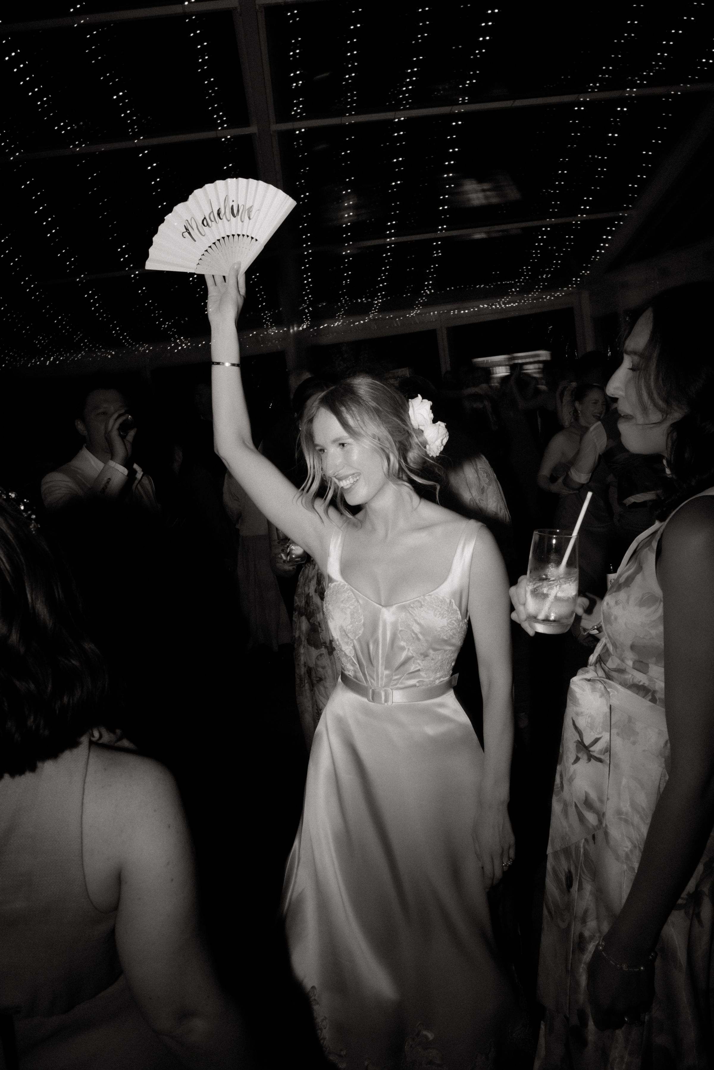 A black and white photo of a bride waving a fan on the dance floor at her wedding.