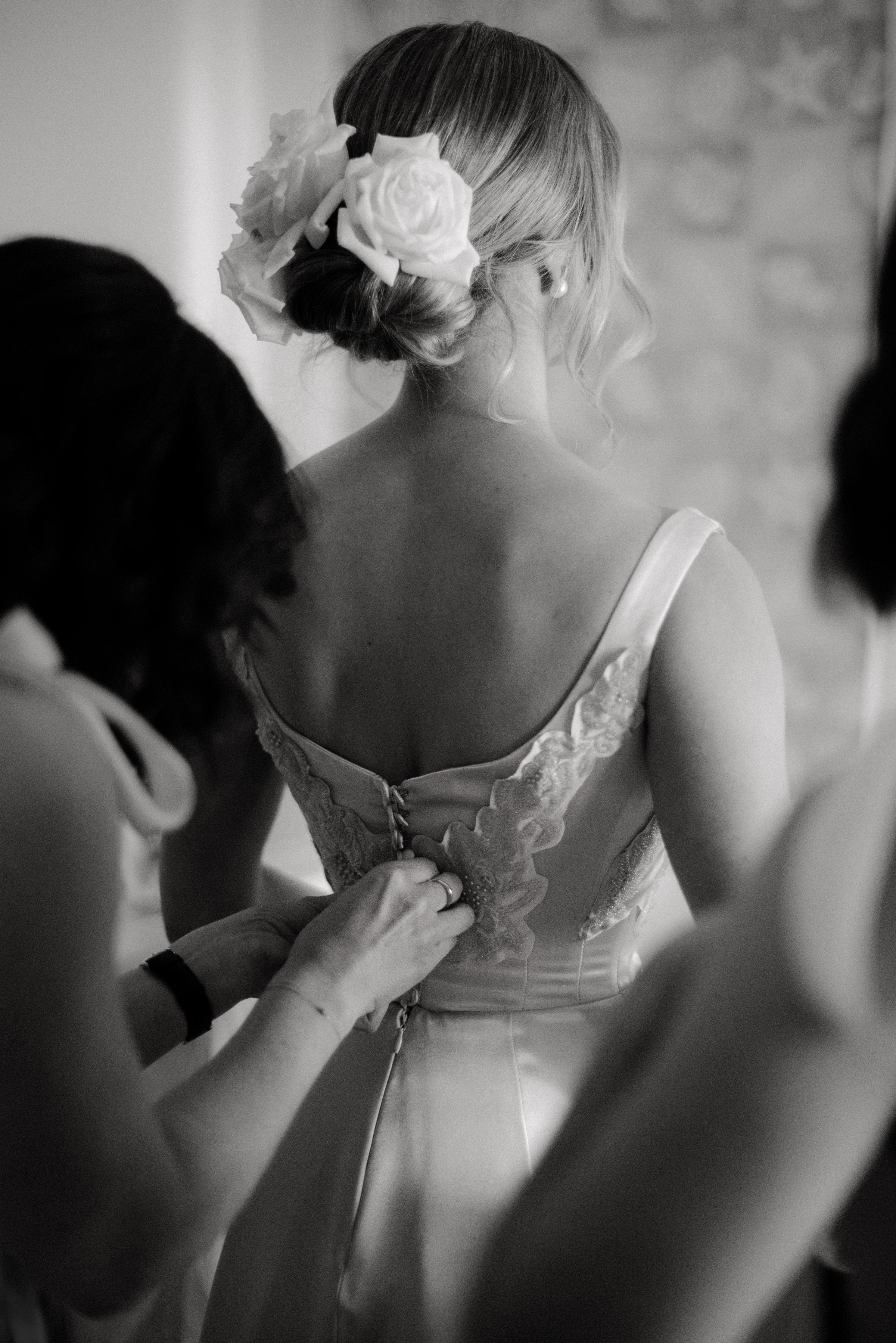 A black and white photo of a bride's dress being laced up by her bridesmaid.